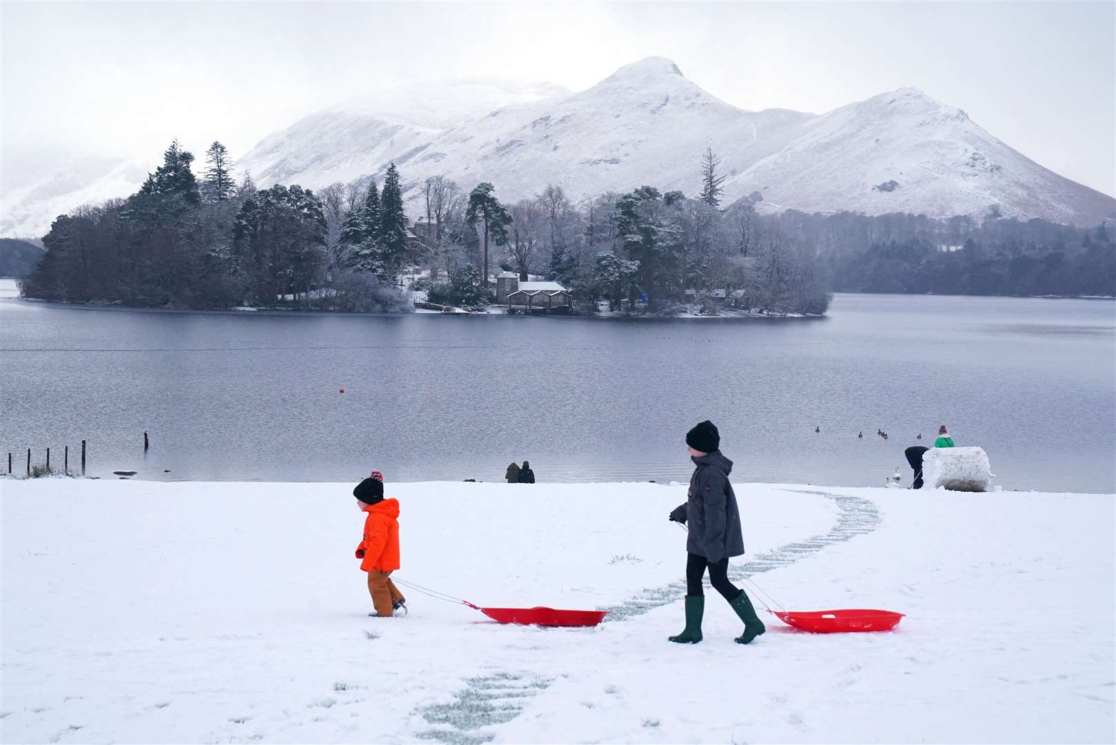 People pulling sledges in snowy conditions in Crow Park at Derwent Water near Keswick, Cumbria (Owen Humphreys/PA)